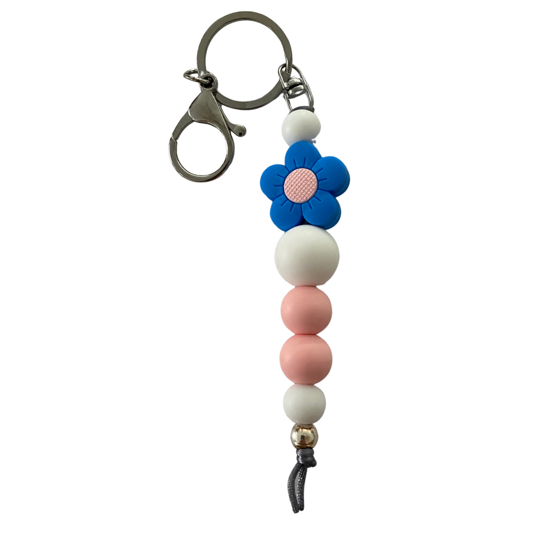 A keyring featuring a bright blue flower silicone bead with other round coloured silicone beads.