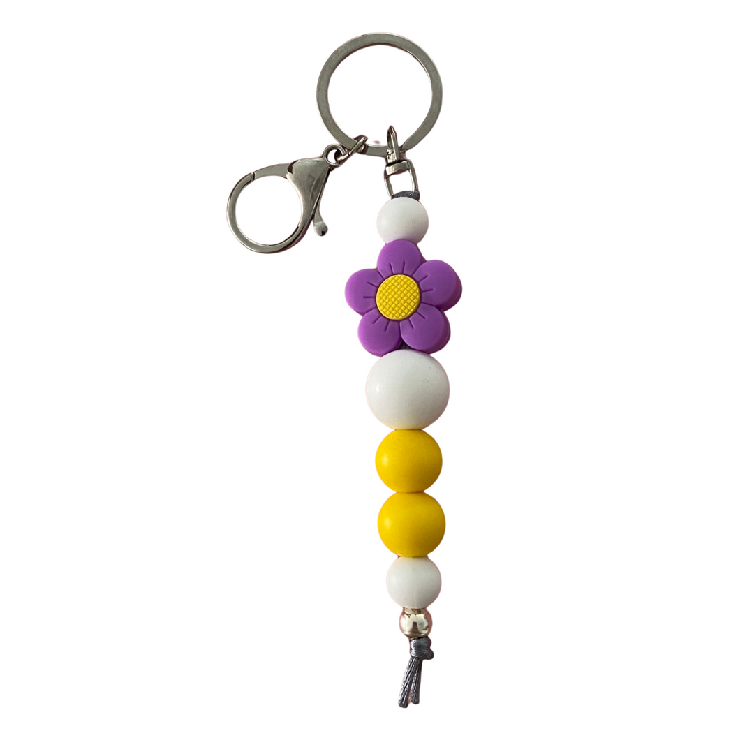 A keyring featuring a bright purple flower silicone bead with other round coloured silicone beads.