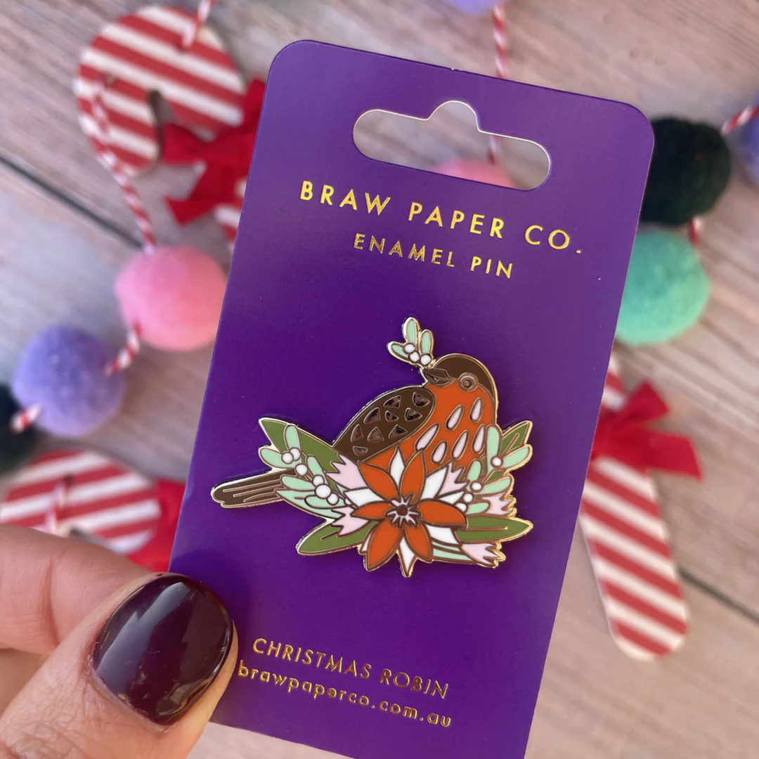 The Christmas Robin Enamel Pin is perched among festive florals and delicate mistletoe.