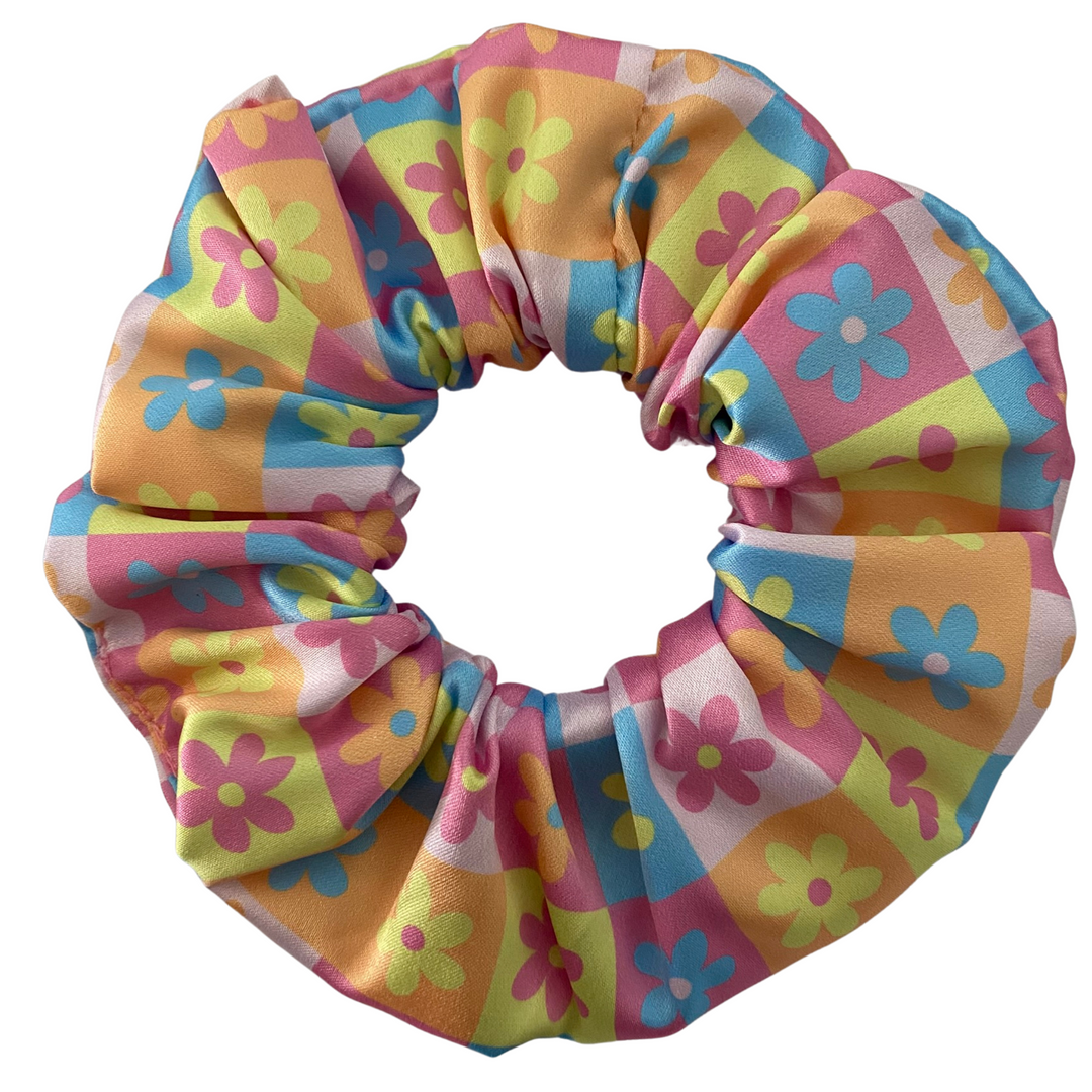 Colourful Daisy Satin Scrunchie. Handmade from soft, shiny stretch satin, this scrunchie features a cheerful patchwork of pink, blue, yellow, and orange daisies.
