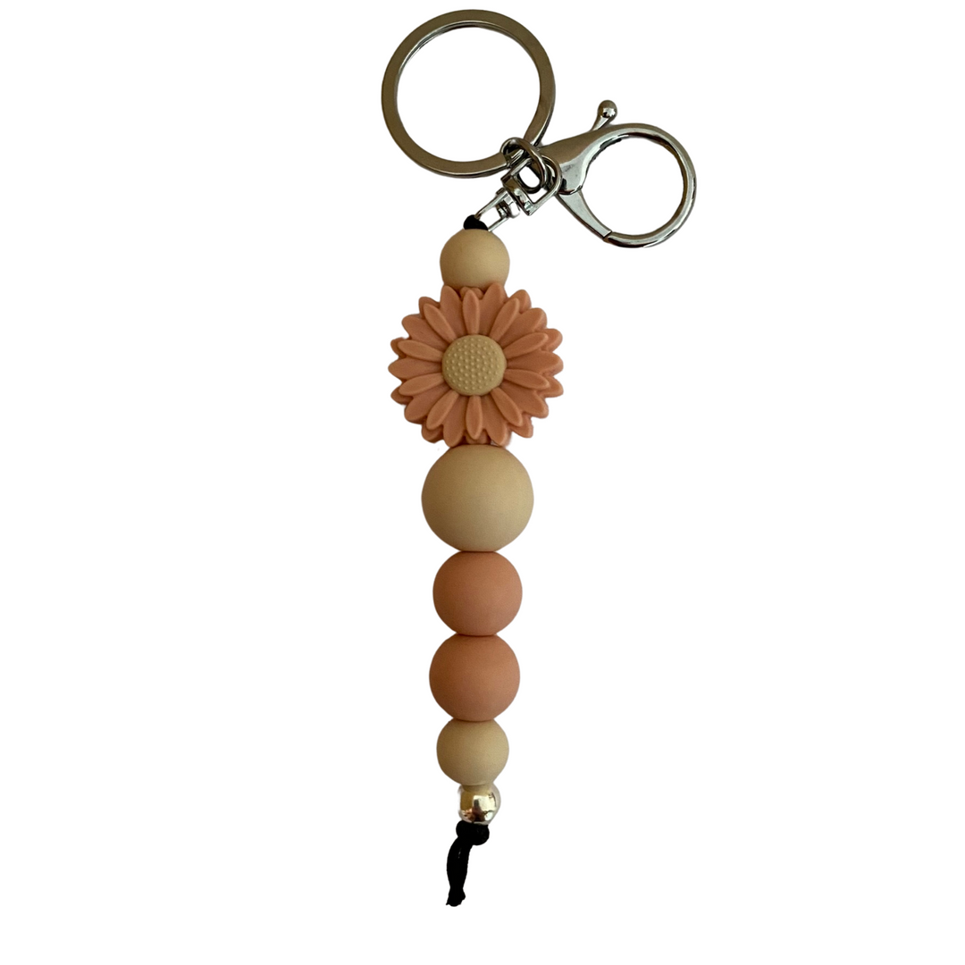 A keyring with a peach daisy silicone bead and other assorted beads.