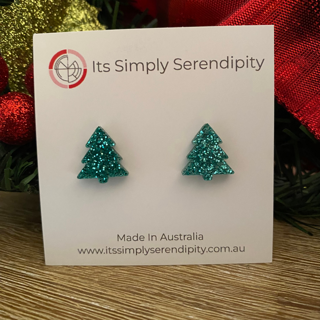 Aqua blue glittery tree-shaped earrings on a 'Its Simply Serendipity' card with Christmas decorations in the background.