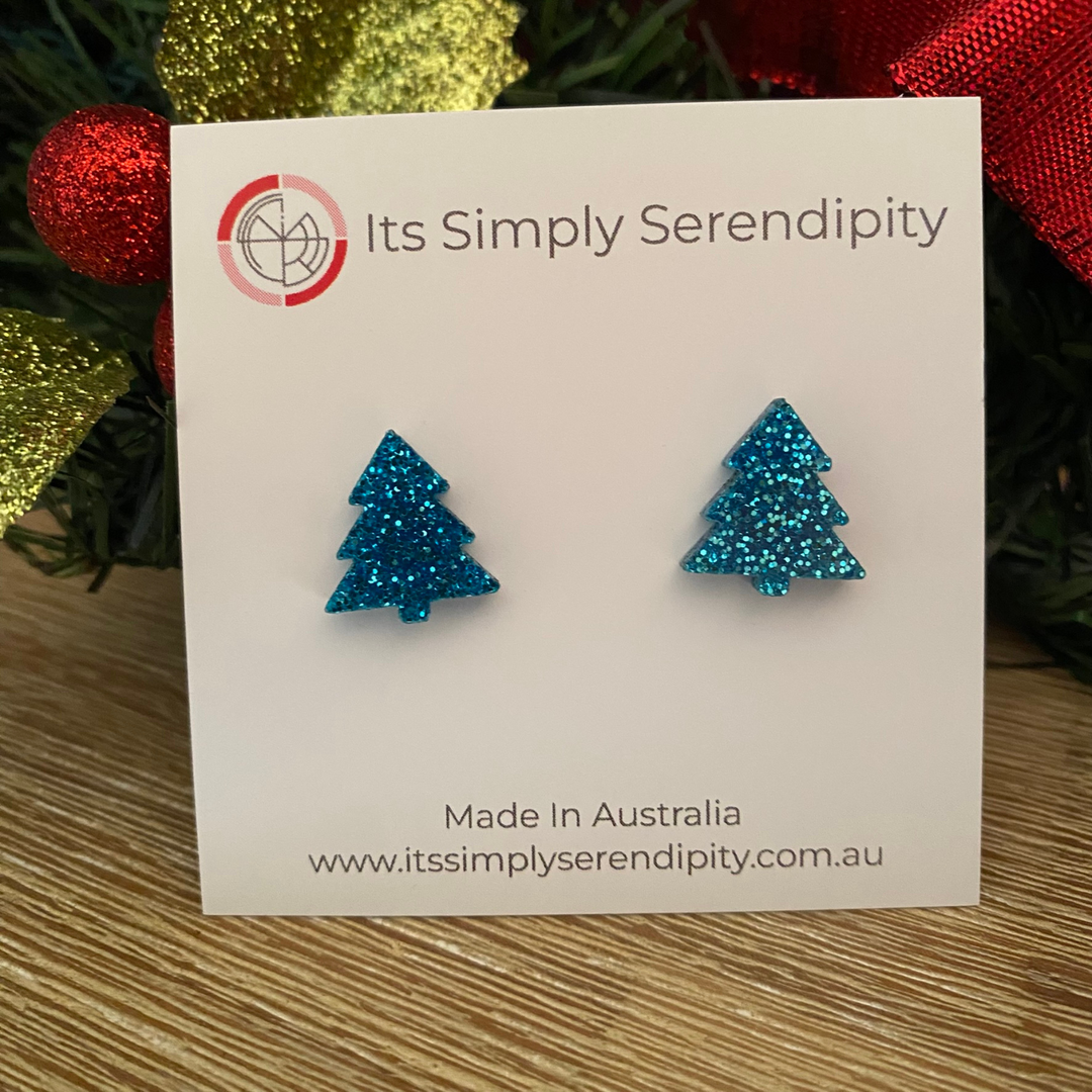 Blue glittery tree-shaped earrings on a 'Its Simply Serendipity' card with Christmas decorations in the background.