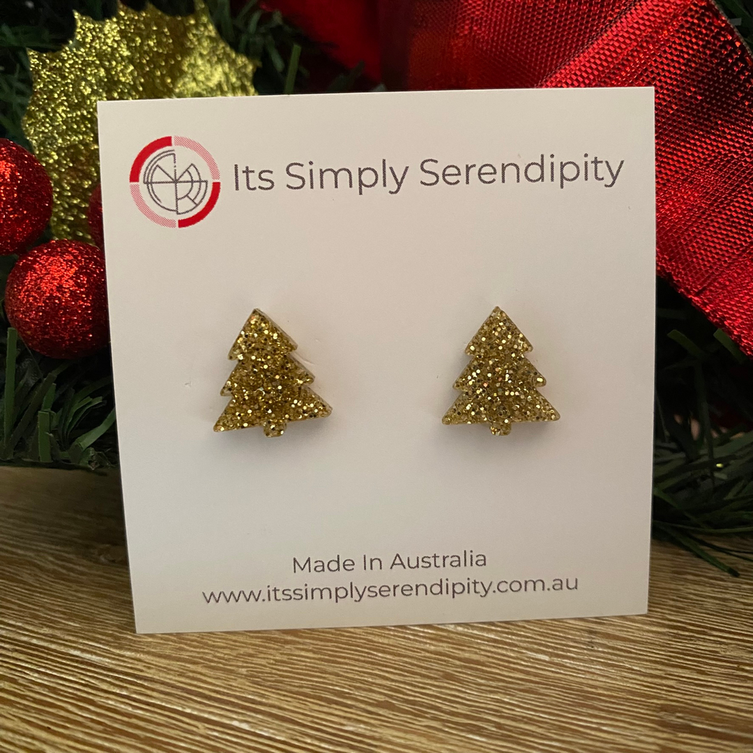 Gold glittery tree-shaped earrings on a 'Its Simply Serendipity' card with Christmas decorations in the background.