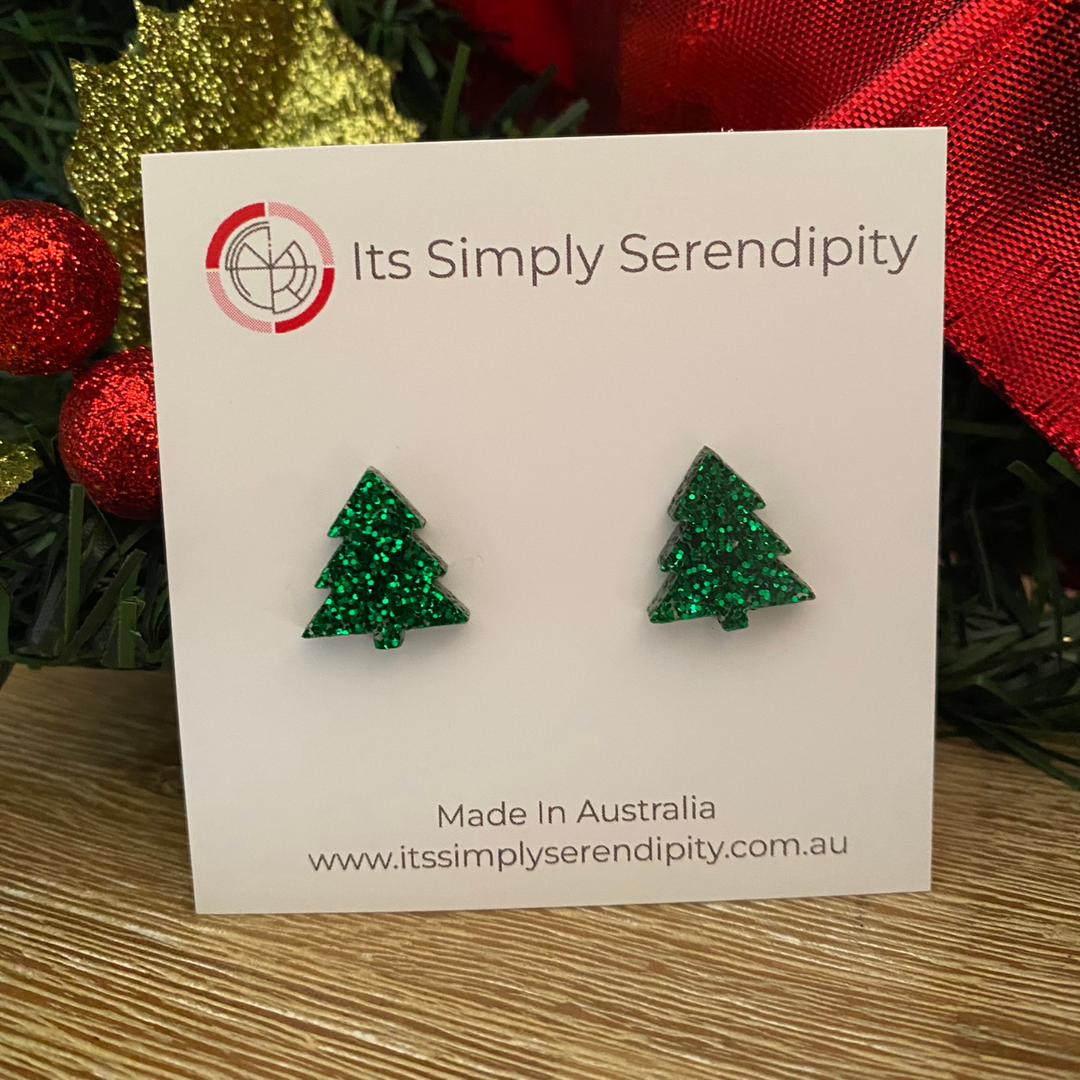 Green glittery tree-shaped earrings on a 'Its Simply Serendipity' card with festive background.