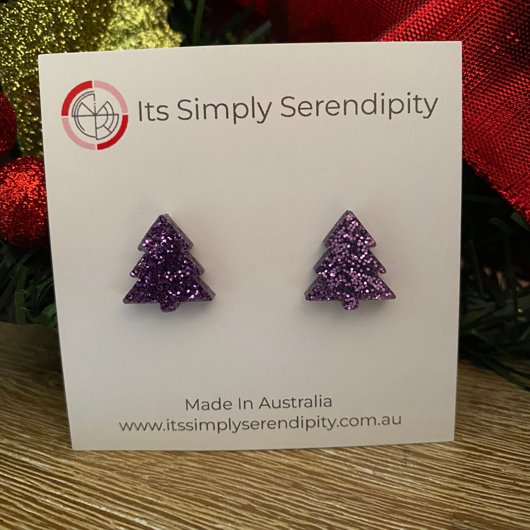 Purple glittery tree-shaped earrings on a 'Its Simply Serendipity' card with Christmas decorations in the background.