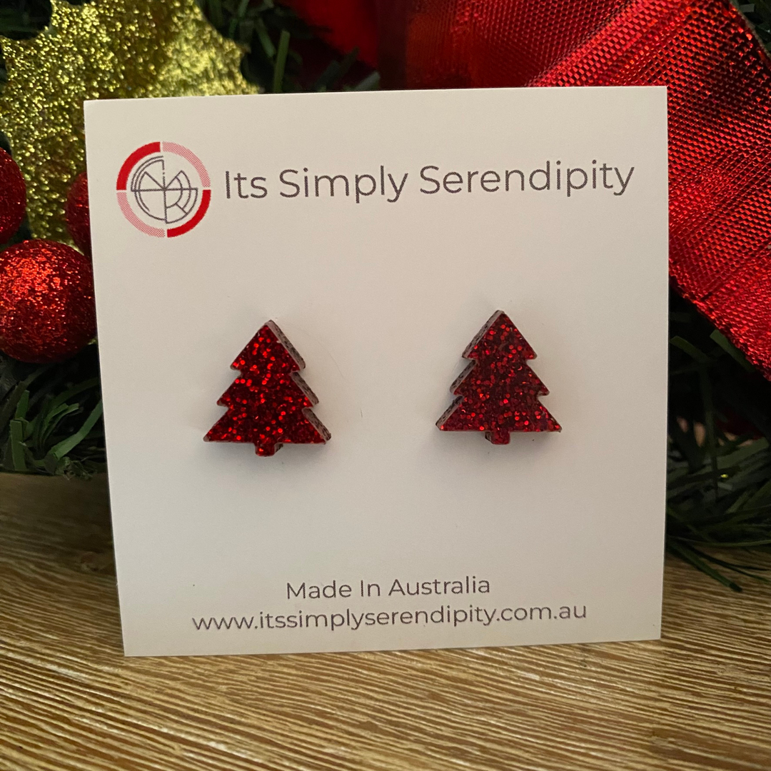 Red glittery tree-shaped earrings on a 'Its Simply Serendipity' card with Christmas decorations in the background.