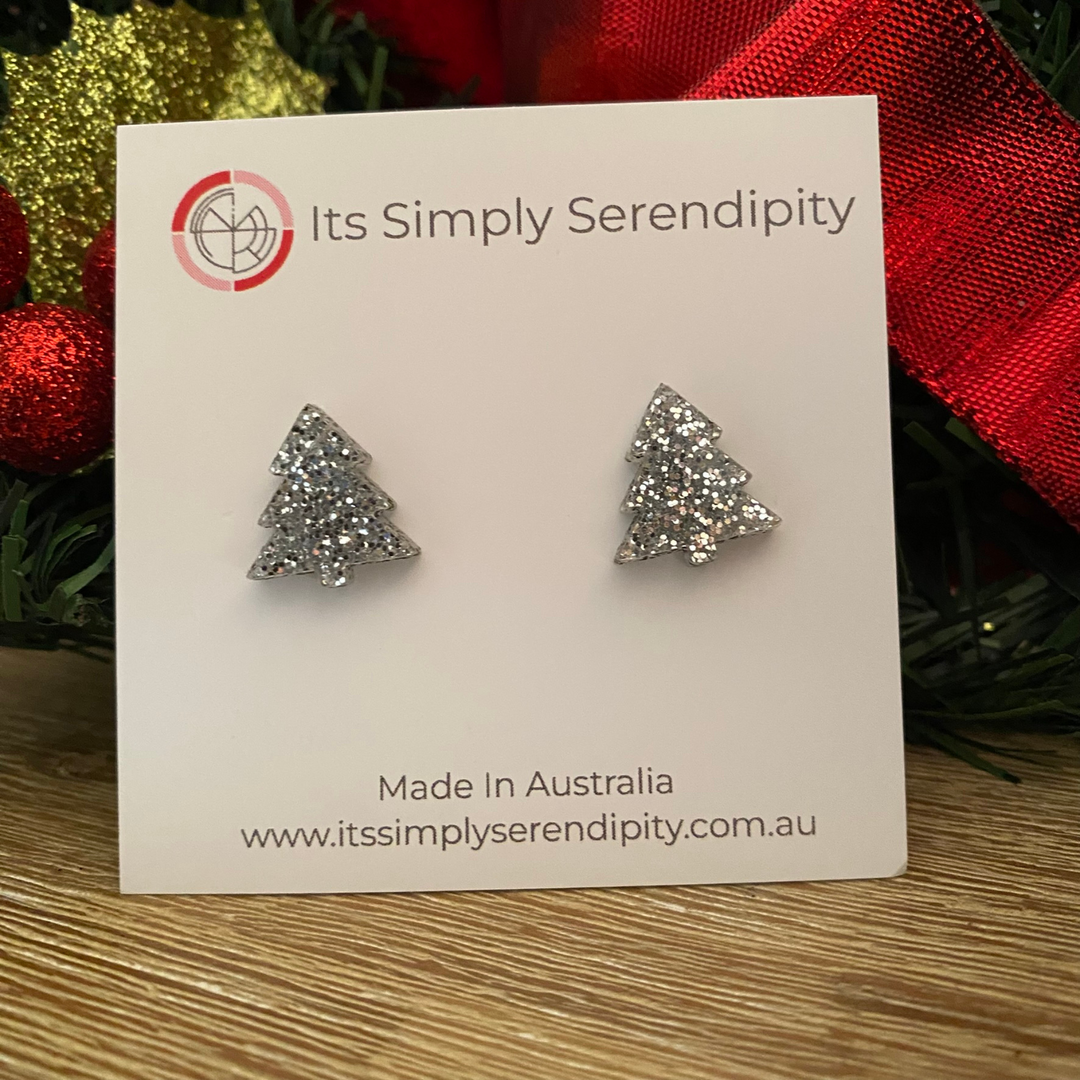 Silver glittery tree-shaped earrings on a 'Its Simply Serendipity' card with Christmas decorations in the background.