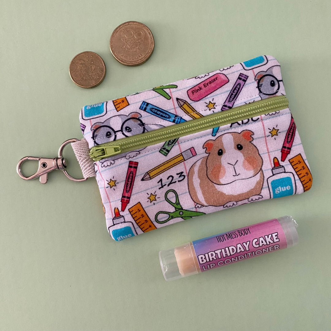 A small clip coin purse perfect for coins and small essentials featuring cute guinea pigs with school accessories on white fabric.