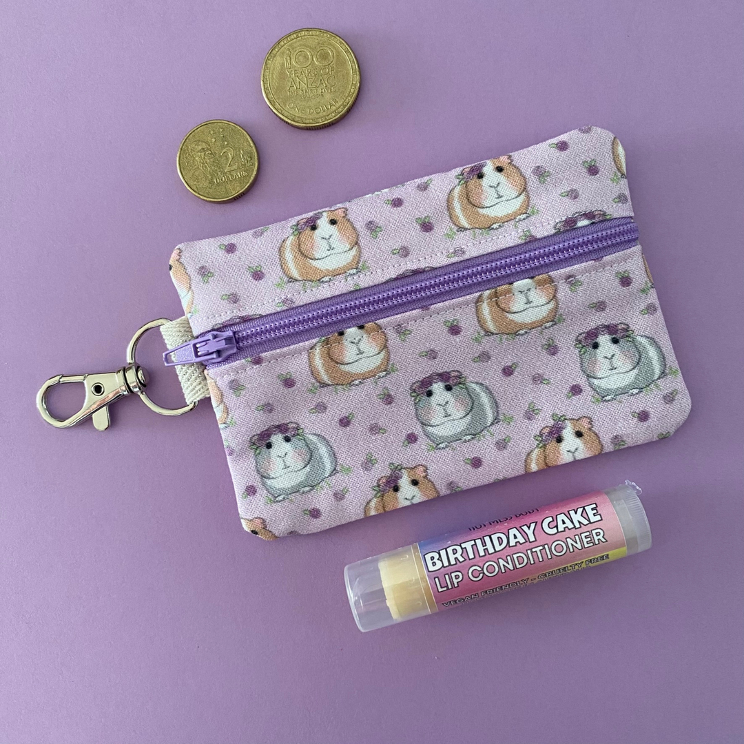 A small clip coin purse perfect for coins and small essentials featuring cute guinea pigs and roses on lilac fabric.