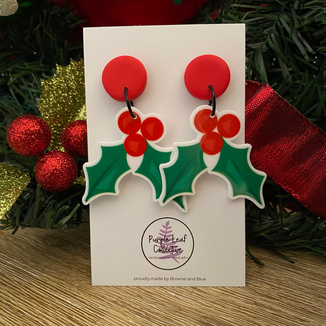 Christmas holly dangle earrings with red stud topper on a white card.