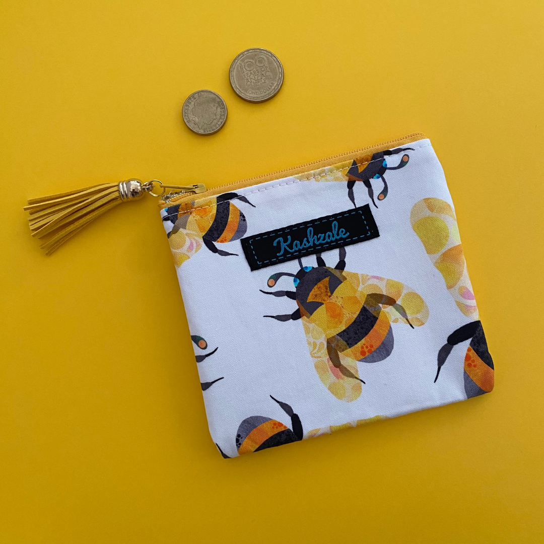 A small coin purse perfect for coins and small essentials featuring yellow bees by Kasey Rainbow on white fabric and a tassel on the zipper.