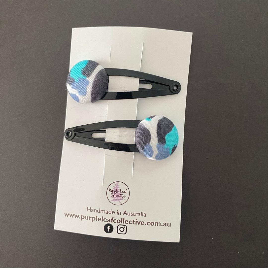 Snow Leopard fabric button hairclips, sold as a set of 2, showcase vibrant fabric designed by Kasey Rainbow. Handmade and ideal for adding a touch of glam to any hairstyle.
