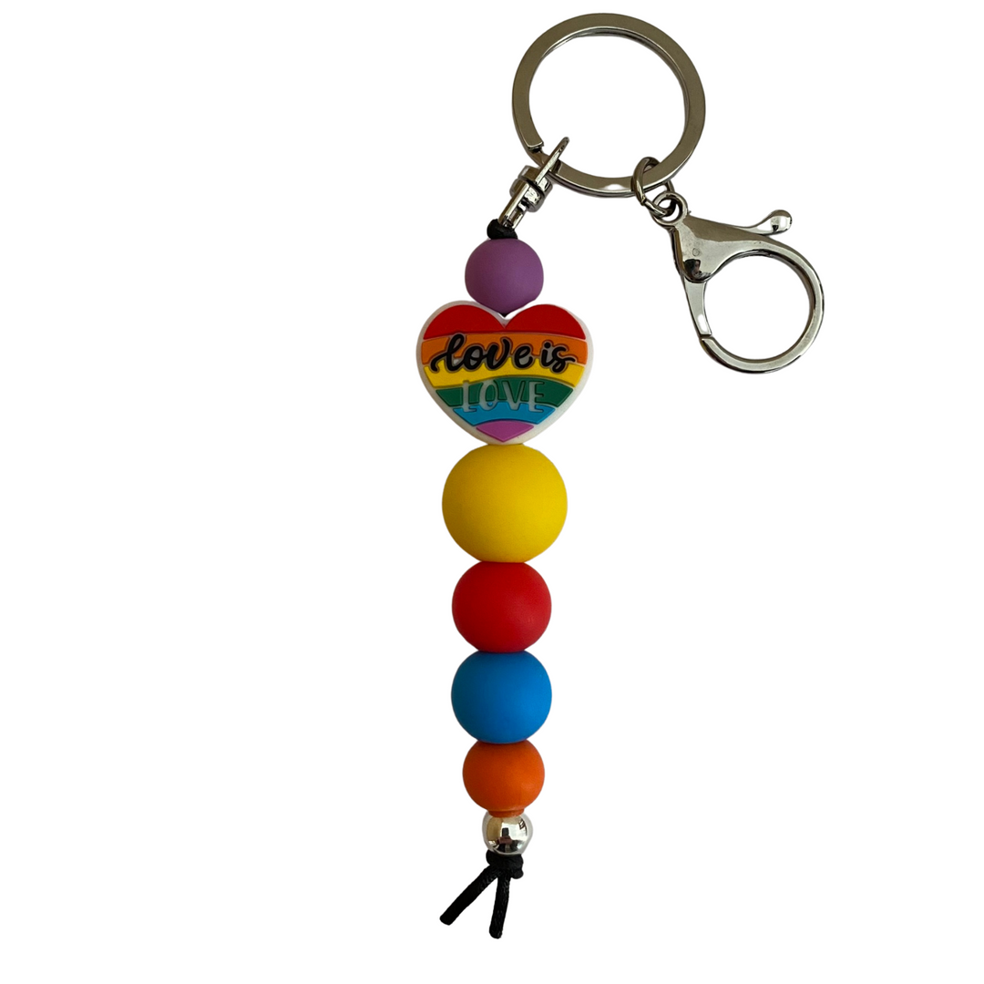 A keyring with a love heart in rainbow colours and the words Love is Love and other round silicone beads.