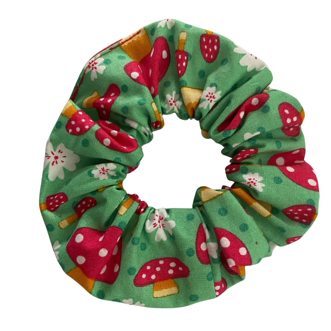 A green fabric scrunchie with red mushrooms. A playful accessory for mushroom lovers and mycology enthusiasts alike!