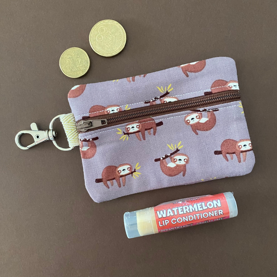A small clip coin purse perfect for coins and small essentials featuring sloths on brown fabric.