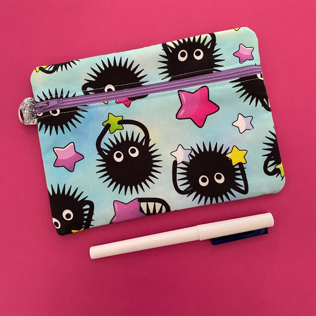 Zipper pouch with images of Soot Sprites playing sport on light blue fabric. Planner accessory for school or work. Perfect for small essentials.