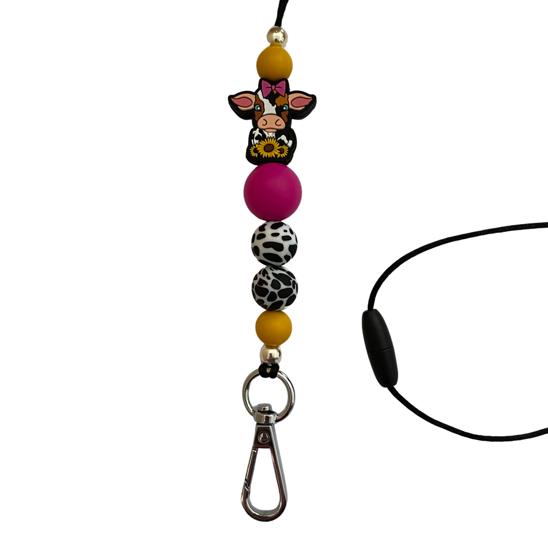 A 60cm lanyard fitted with a safety break away clasp and a cow with a pink bow and sunflowers silicone bead and other coloured round silicone beads.