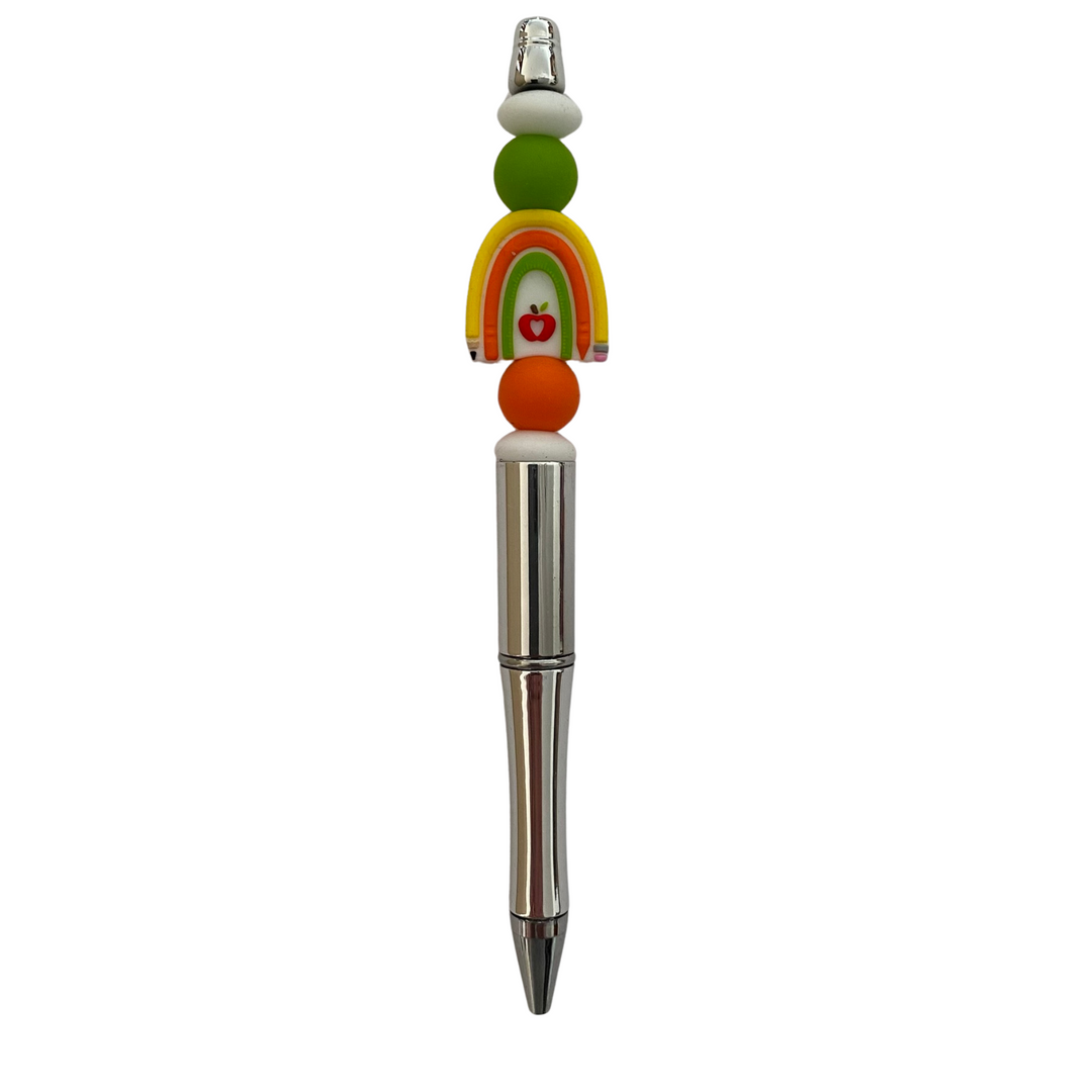 A black ink refillable pen. the Teacher's Sunshine Yellow Rainbow Pen features a silicone rainbow bead inspired by a classic pencil and eraser, complete with a bright red apple at its centre.