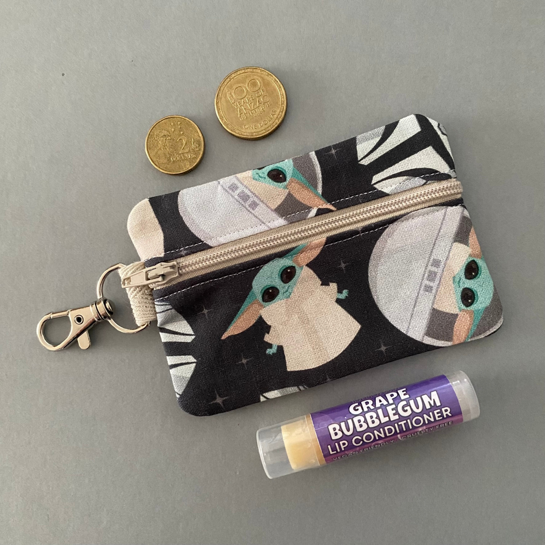 A small clip coin purse perfect for coins and small essentials featuring the Mandalorian and Grogu on black fabric.