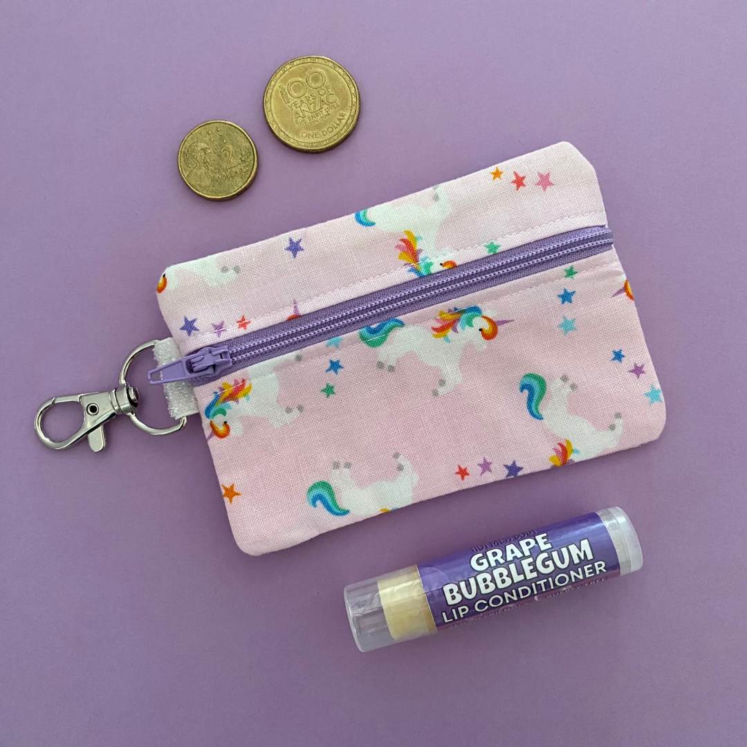 A small clip coin purse perfect for coins and small essentials featuring magical unicorns and stars on pink fabric.