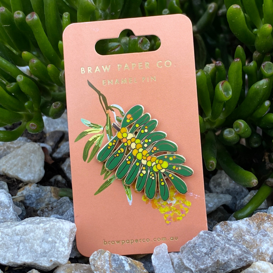 Exquisite Acacia Enamel Pin, showcasing intricate details and vibrant colours of greens, yellows and oranges inspired by this iconic Australian flower.