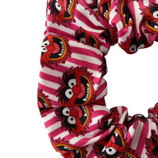 Close up view of a scrunchie with pink and white stripes and red animal puppet character pattern on a white background.