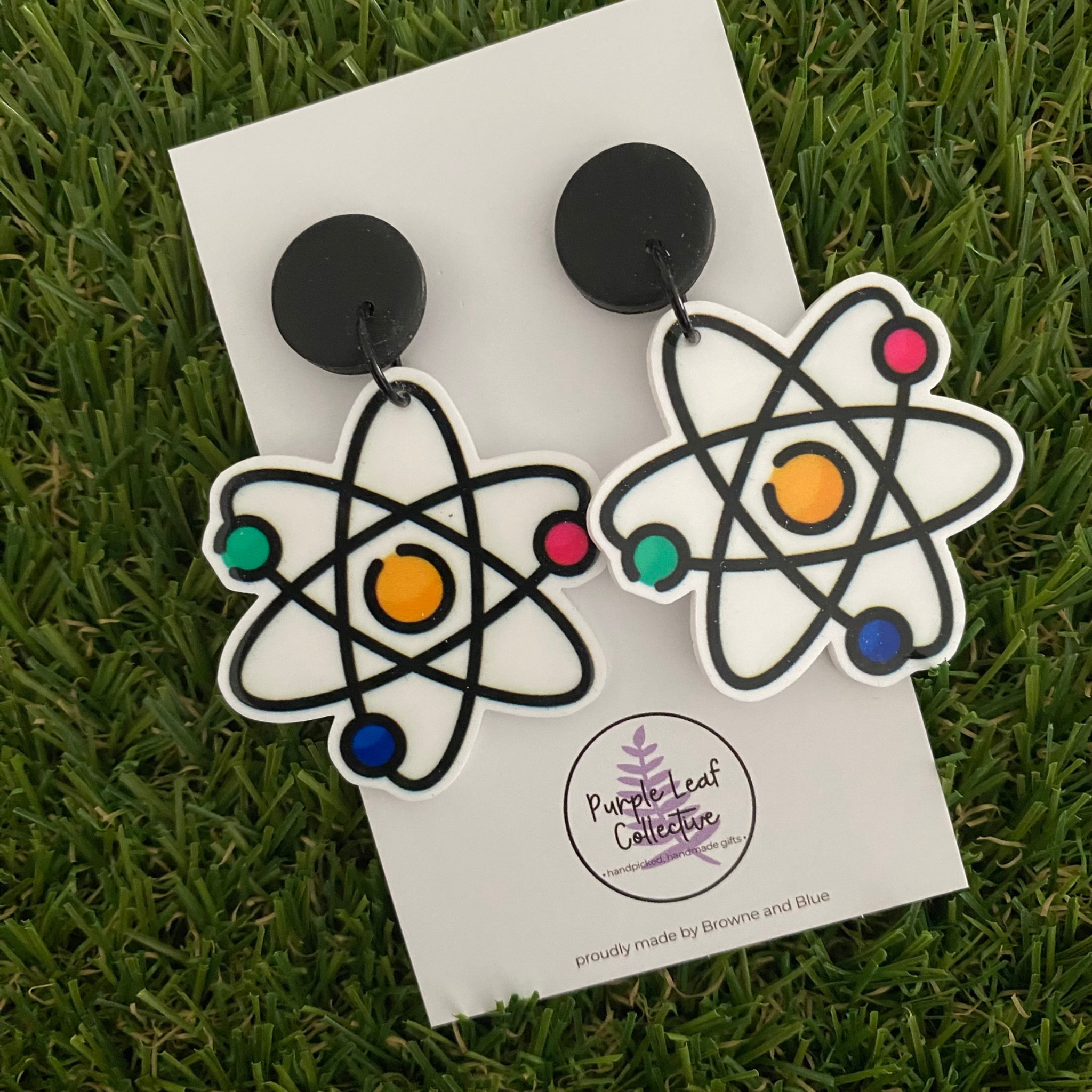 A pair of atomic themed earrings on white backing card.