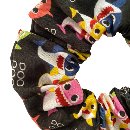 Close up view of a black fabric scrunchie with colourful images of baby shark family and Doo Doo wording.