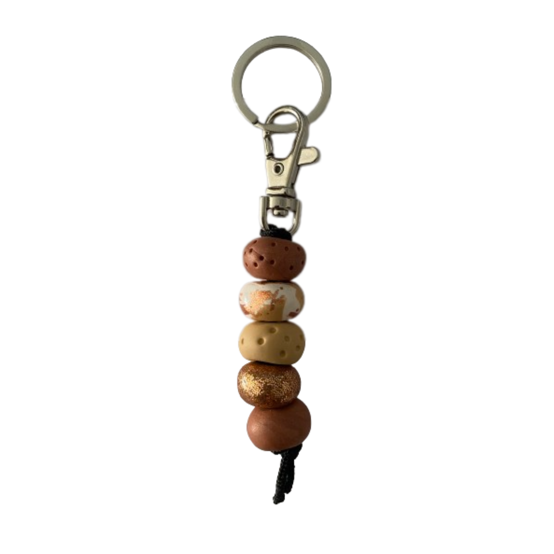 Handmade polymer clay keyring featuring five hand-rolled beads in a mix of brown, mustard and intricate patterns with gold foil design, attached to a silver clasp.