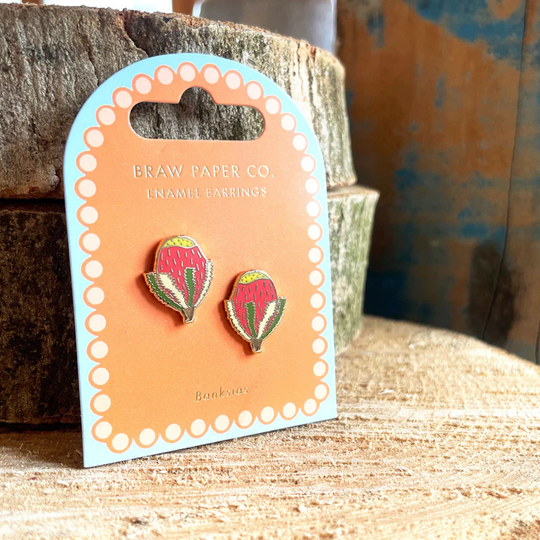 A pair of Banksia enamel stud earrings on a branded card with a rustic background.