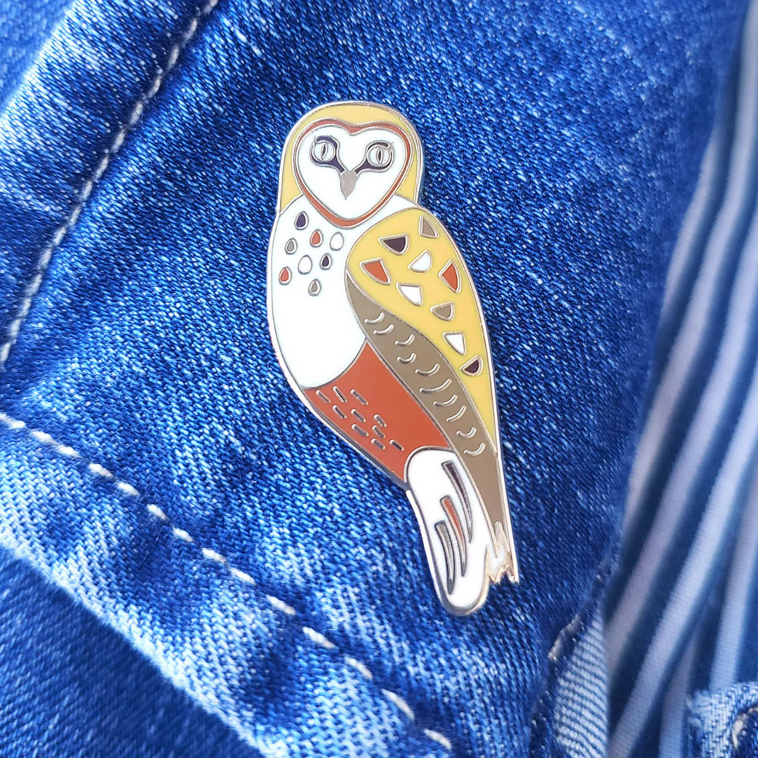 A picture of the Barn Owl Enamel Pin pinned to a denim jacket.
