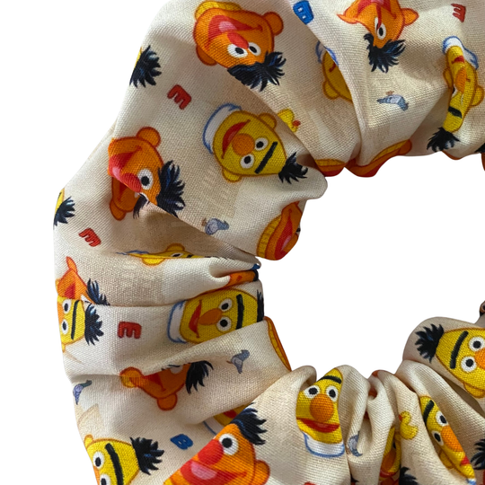 Close up view of a cream coloured scrunchie featuring images of Bert& Ernie along with rubber duckie and Bernice.