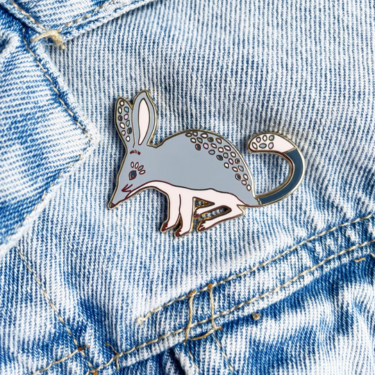 A picture of a Bilby enamel pin syled on a denim jacket.