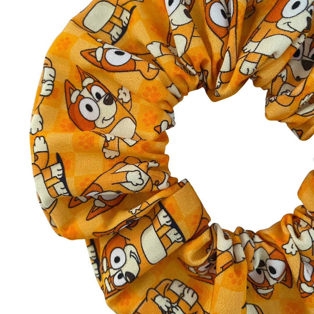 Close up view of a handmade Bingo scrunchie featuring a repeating pattern of Bingo on a vibrant orange fabric.