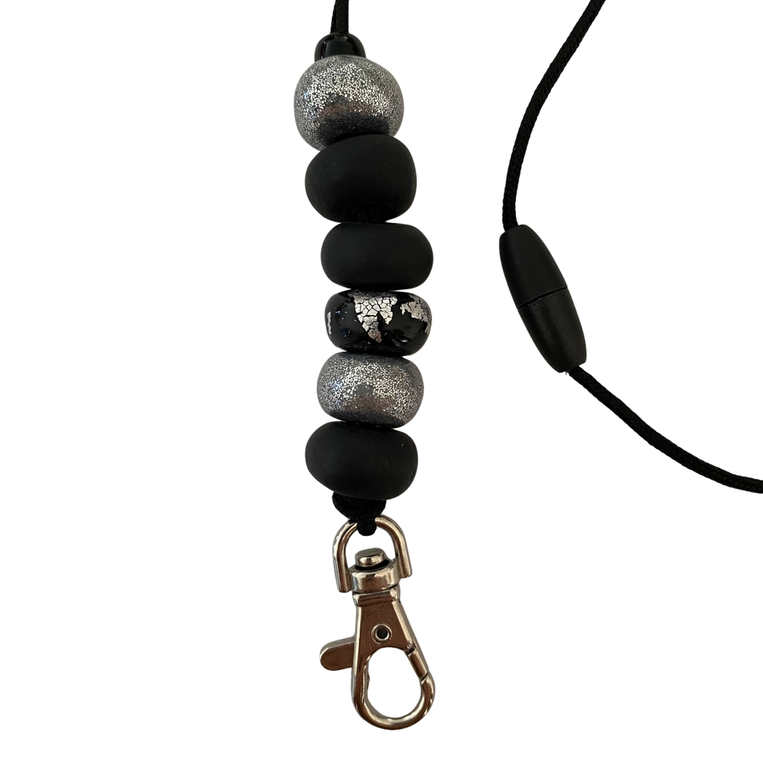 Close-up of six unique, handmade polymer clay beads in silver and black on a lanyard cord with a breakaway safety clasp and a silver-plated clip.