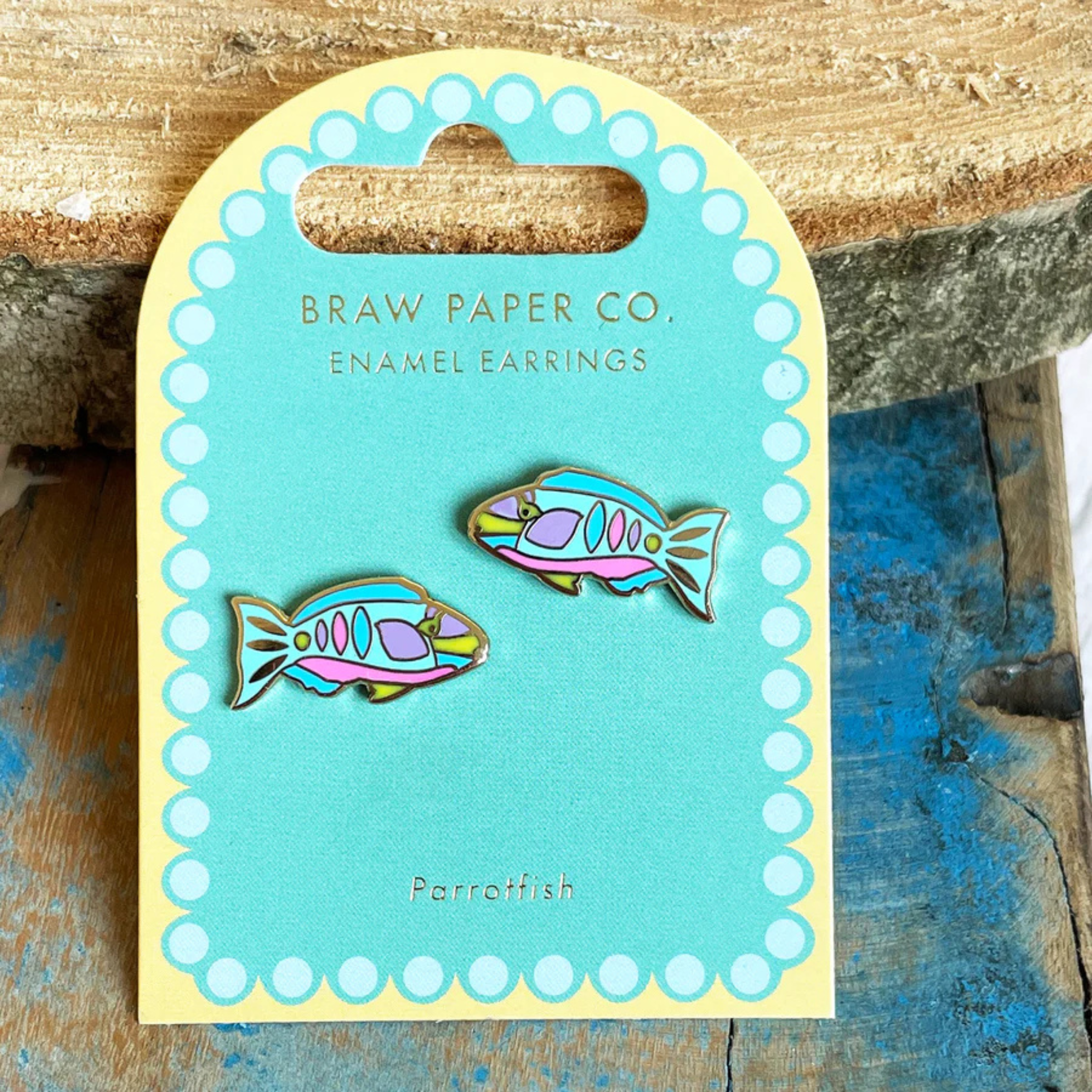 Enamel earrings of parrotfish on a Braw Paper Co. card against a rustic wooden background.