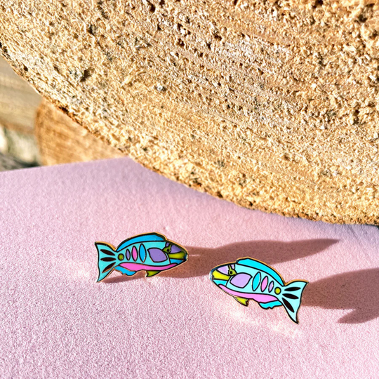 Colourful fish-shaped earrings on a pink surface with a beige background.