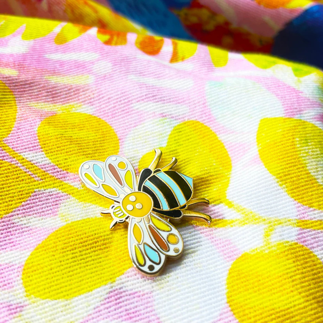 Colourful bee-shaped pin on a floral fabric background.