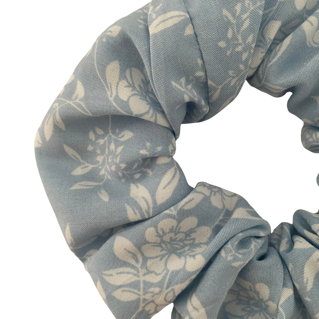Close up view of a blue rayon scrunchie featuring an elegant two-toned floral pattern in shades of blue and white.