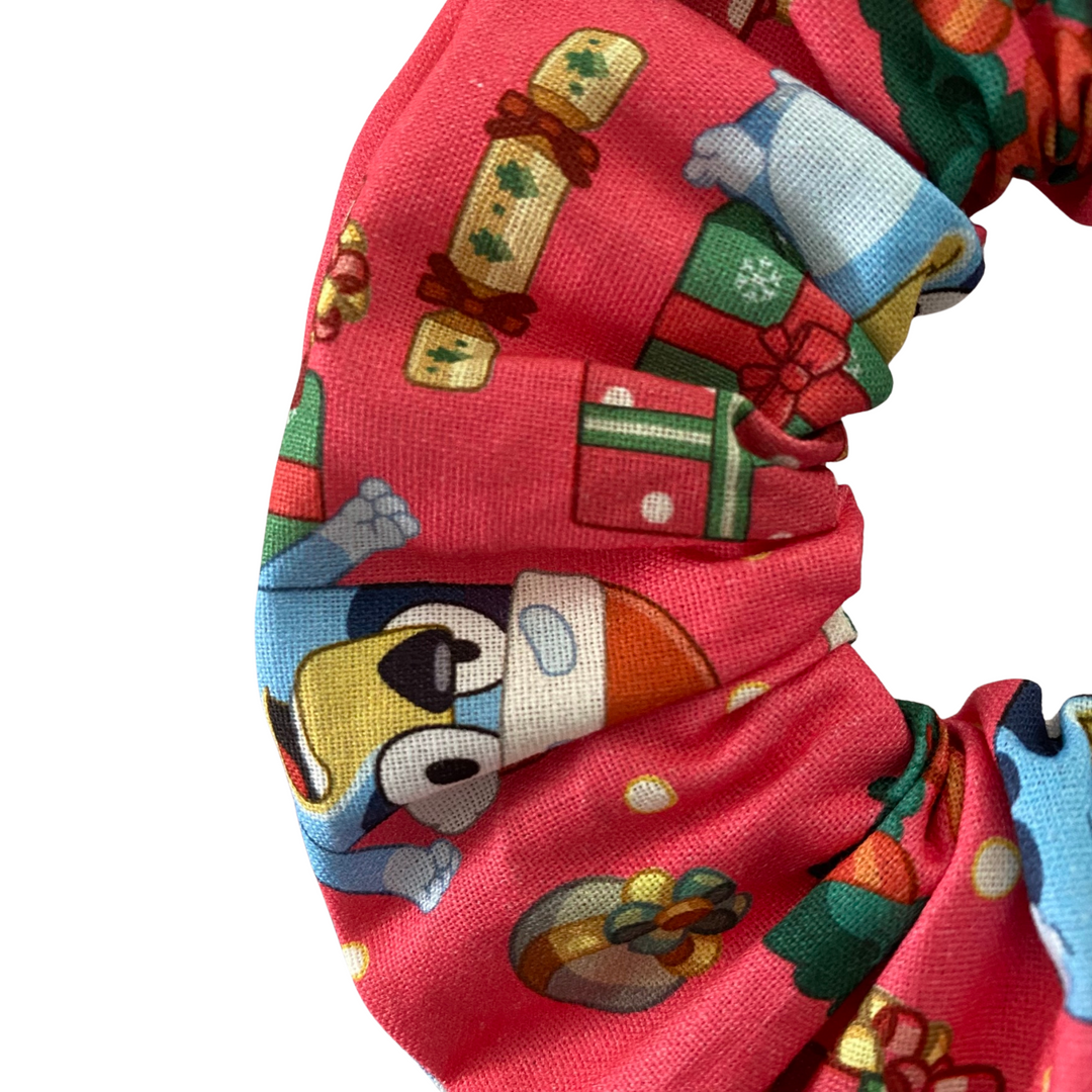 Close up view of a red scrunchie with Bluey and Bingo character pattern on a white background.