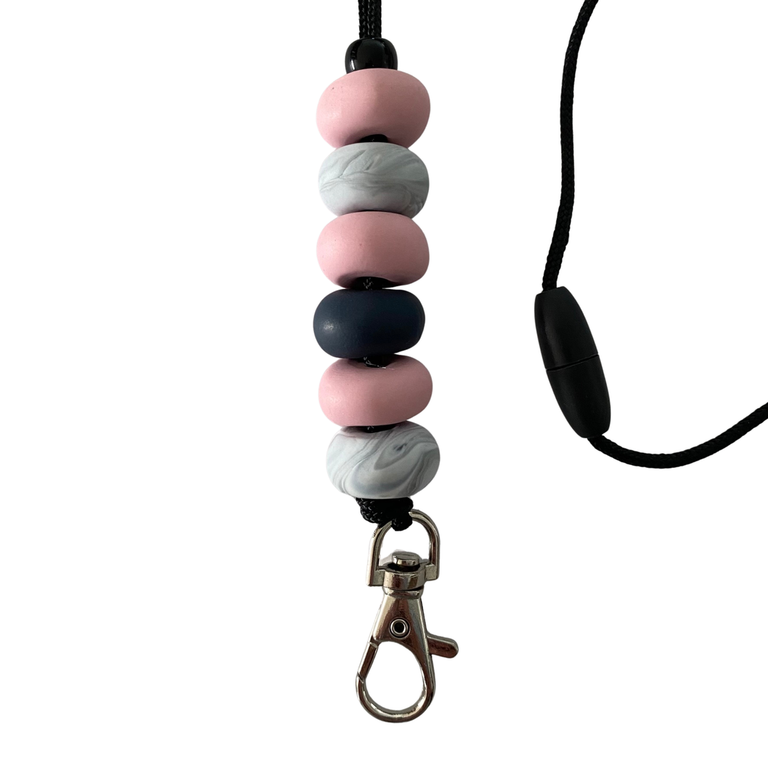 Close-up of six unique, handmade polymer clay beads in pink, navy blue, and marbled effects on a lanyard cord with a breakaway safety clasp and a silver-plated clip.