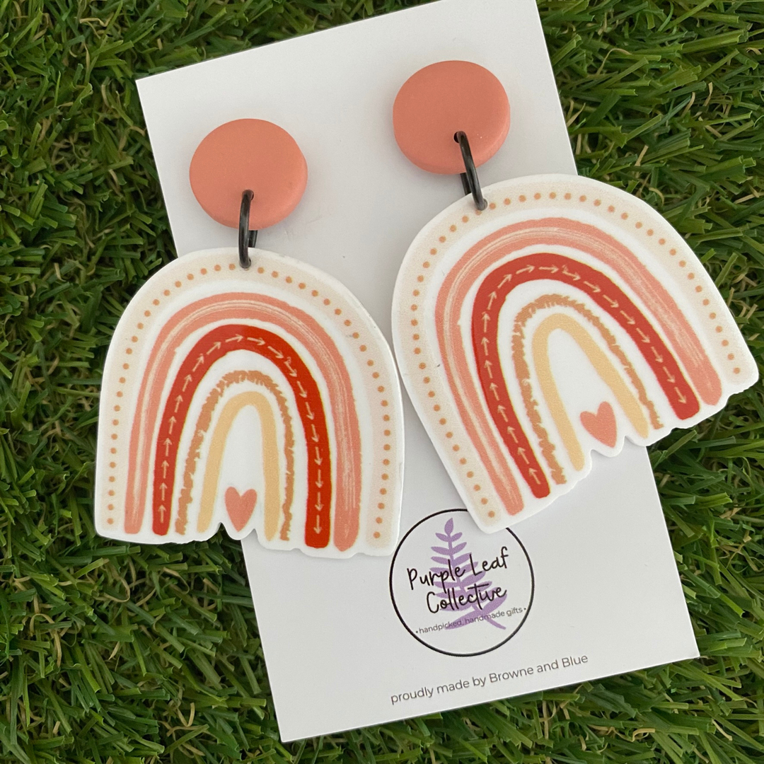 Rainbow-shaped earrings featuring a arch design in earthy clay tones with a love heart at the base, all set on peach clay tops