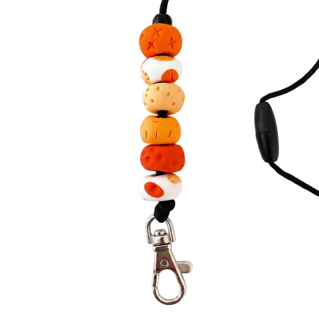 Handmade polymer clay lanyard with six hand-rolled beads in orange colours. Threaded on a nylon cord with a breakaway safety clasp and a silver-plated clip.