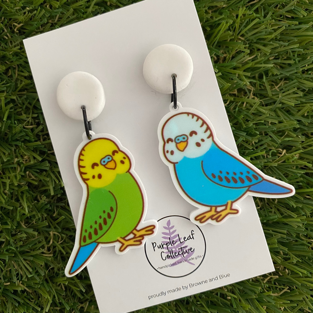 Dangle earrings featuring a pair of yellow and blue Budgies on white clay tops.