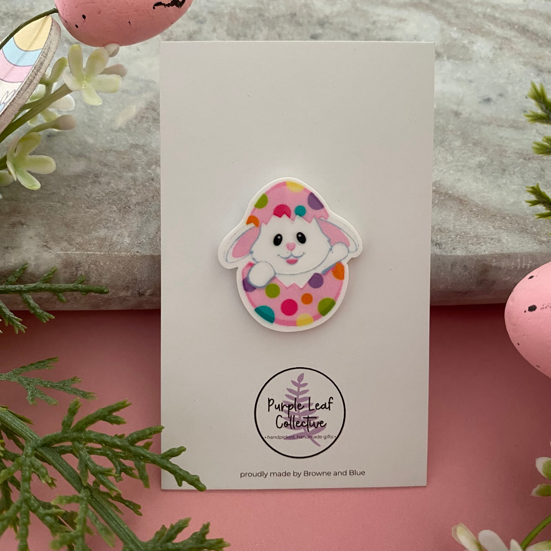 A Easter brooch featuring a cute white bunny peeking out of a colourful spotted Easter egg.