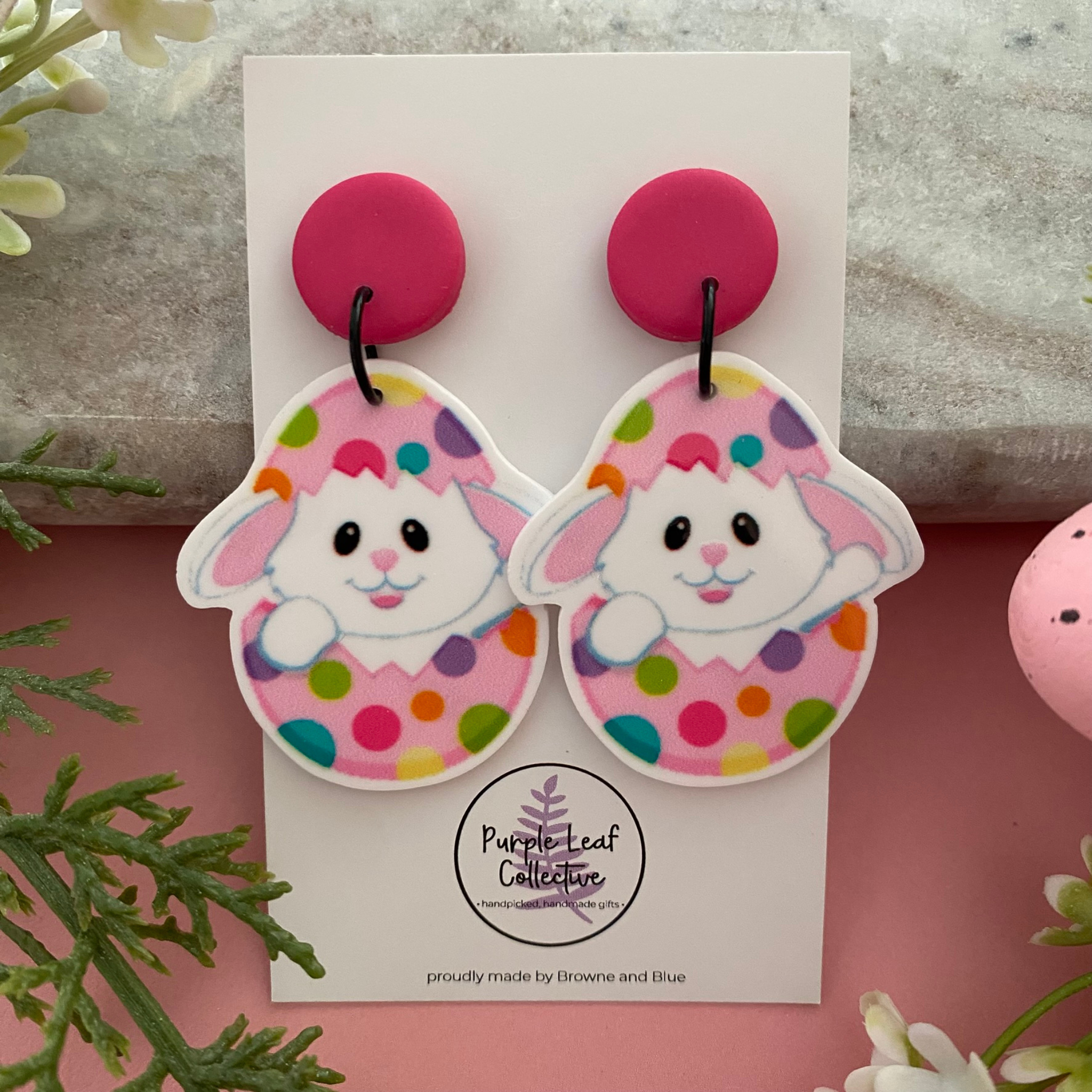 A pair of handmade dangle earrings featuring a cute white bunny peeking out of a colourful spotted Easter egg, attached to comfortable stud backs.