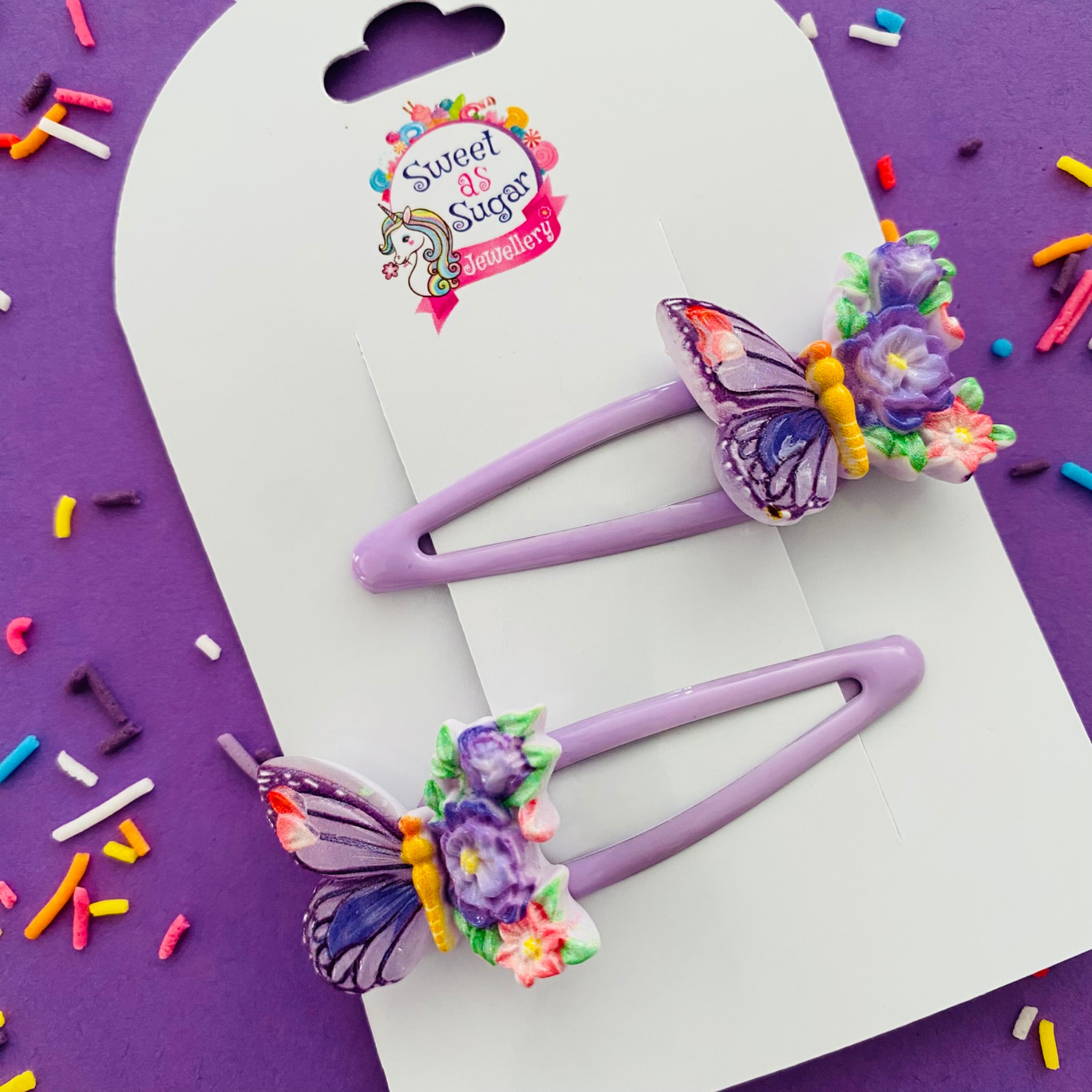 A pair of lavender snap clips with a lavender winged butterfly and flowers.