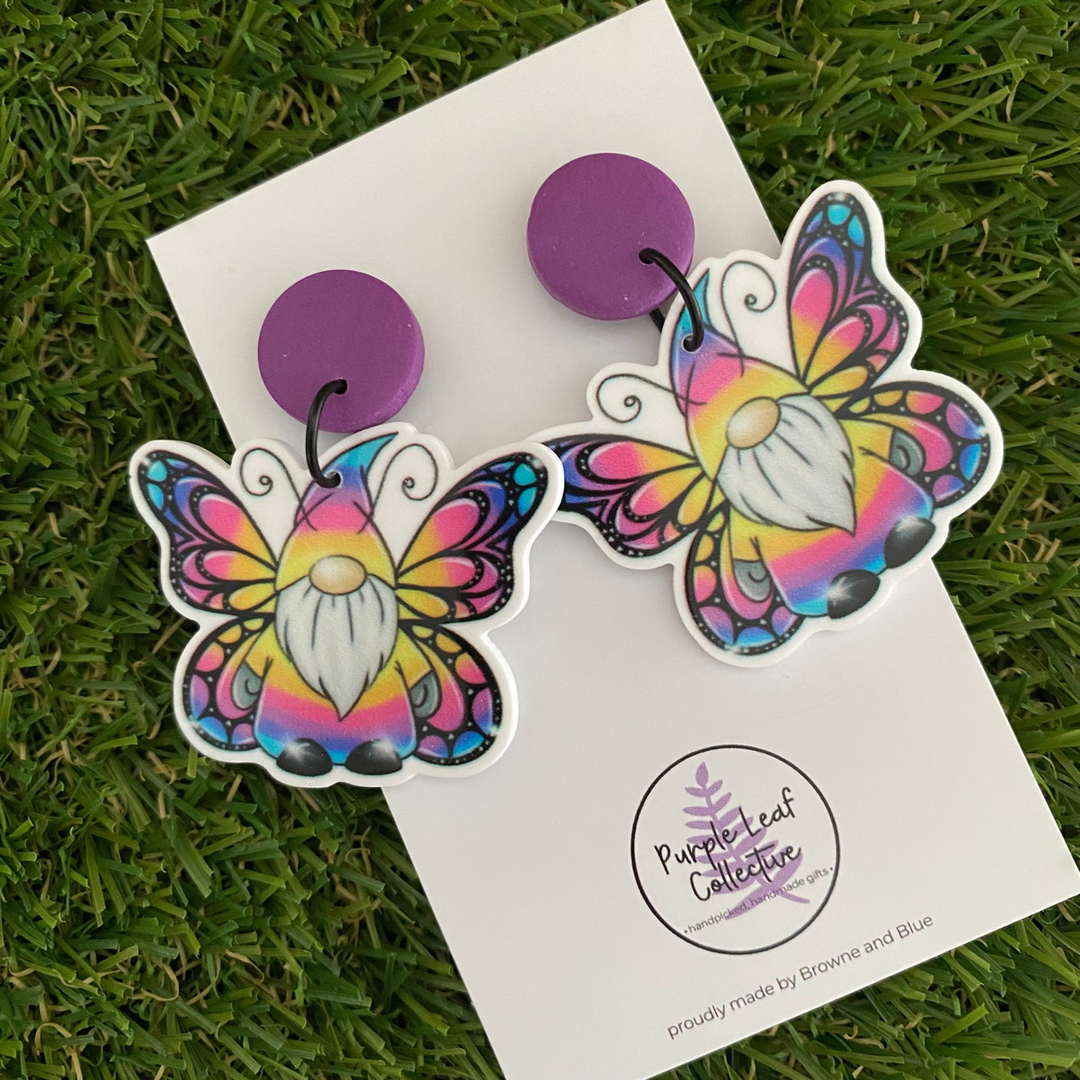 Dangle earrings, featuring two gnomes with purple, blue, and yellow butterfly wings set on matching purple clay tops.