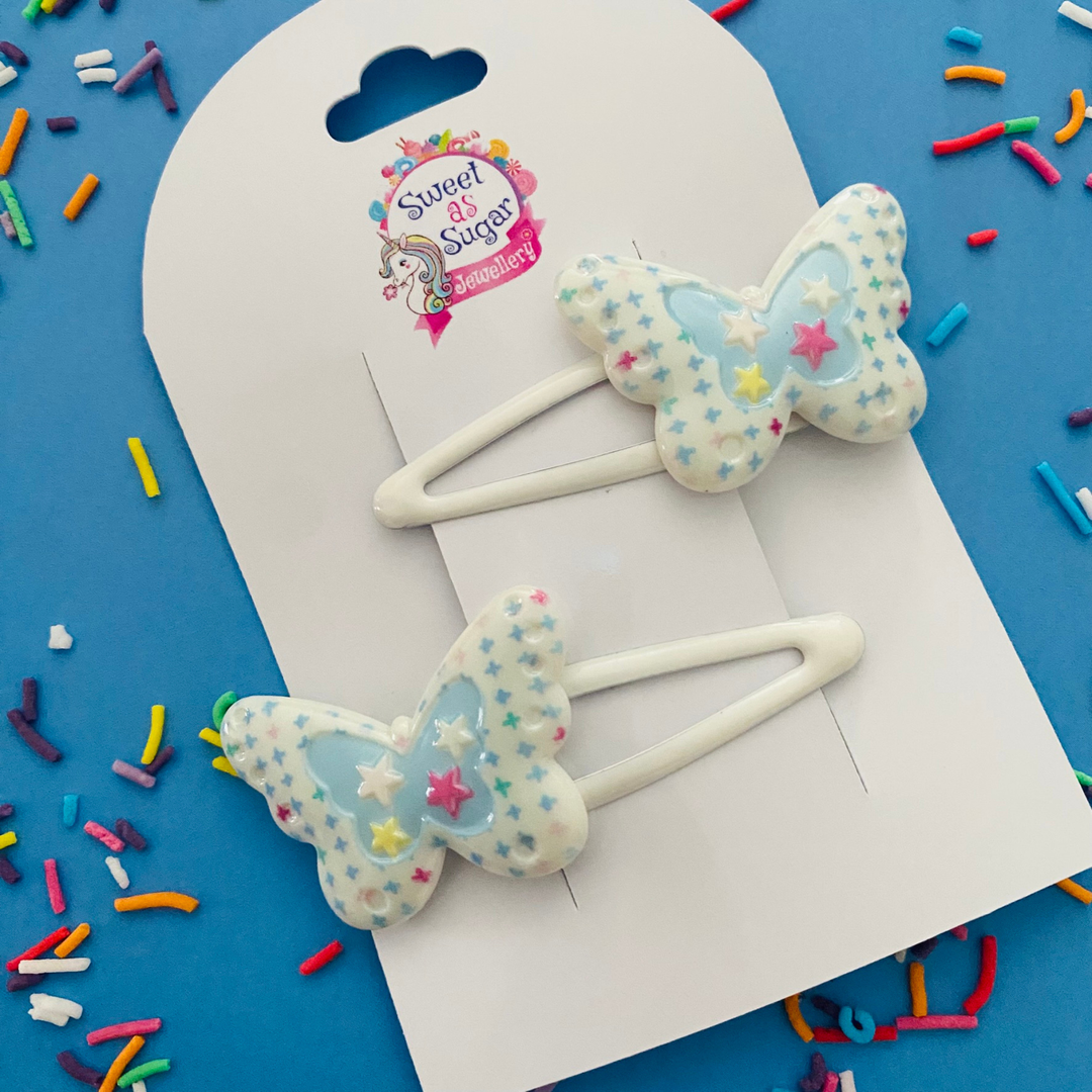 A pair of white snap clips featuring a blue starred butterfly charm.